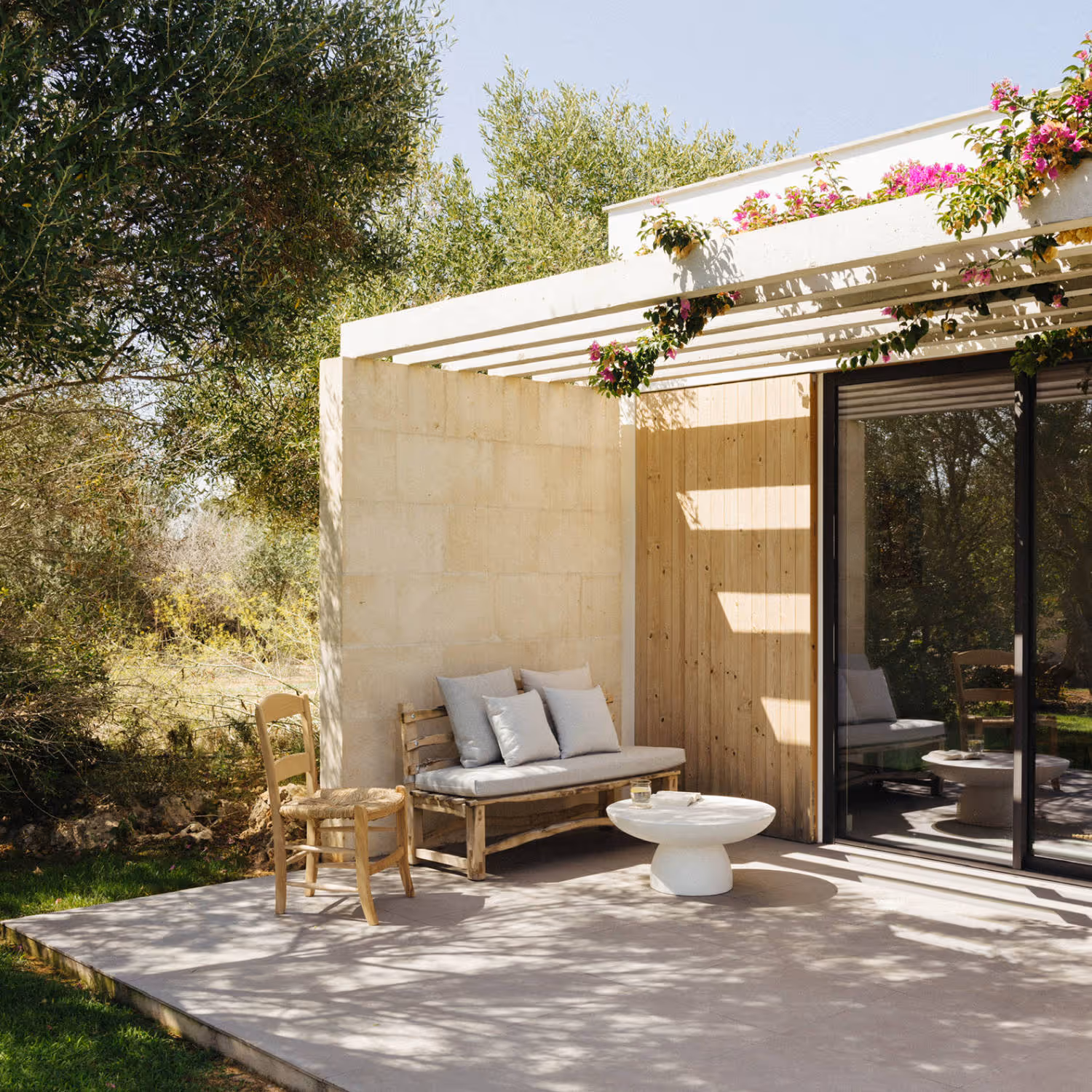 Solutions for every need: Image that shows a cozy terrace under a pergola covered by a bougainvillea plant. The terrace is surrounded by nature and has a wooden sofa and chair that transmit comfort and peace.