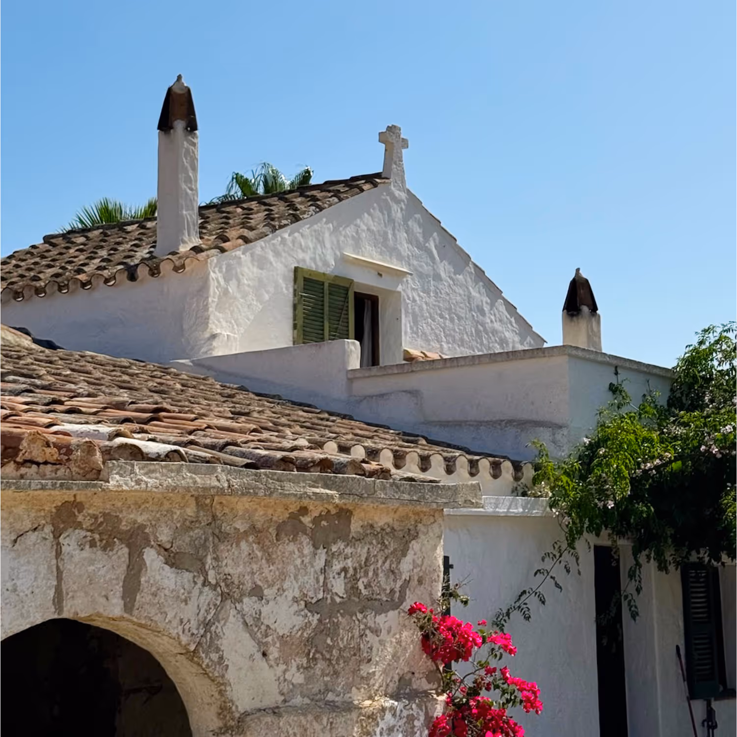 Services, purchase. Image showing a traditional Menorcan house with white mares walls and terracotta Arabic tiled roof. The house has a charming bignonia and bougainvillea plant in the façade.
